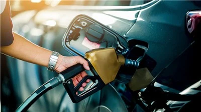 Person holding a fuel pump nozzle to refuel a vehicle at a gas station