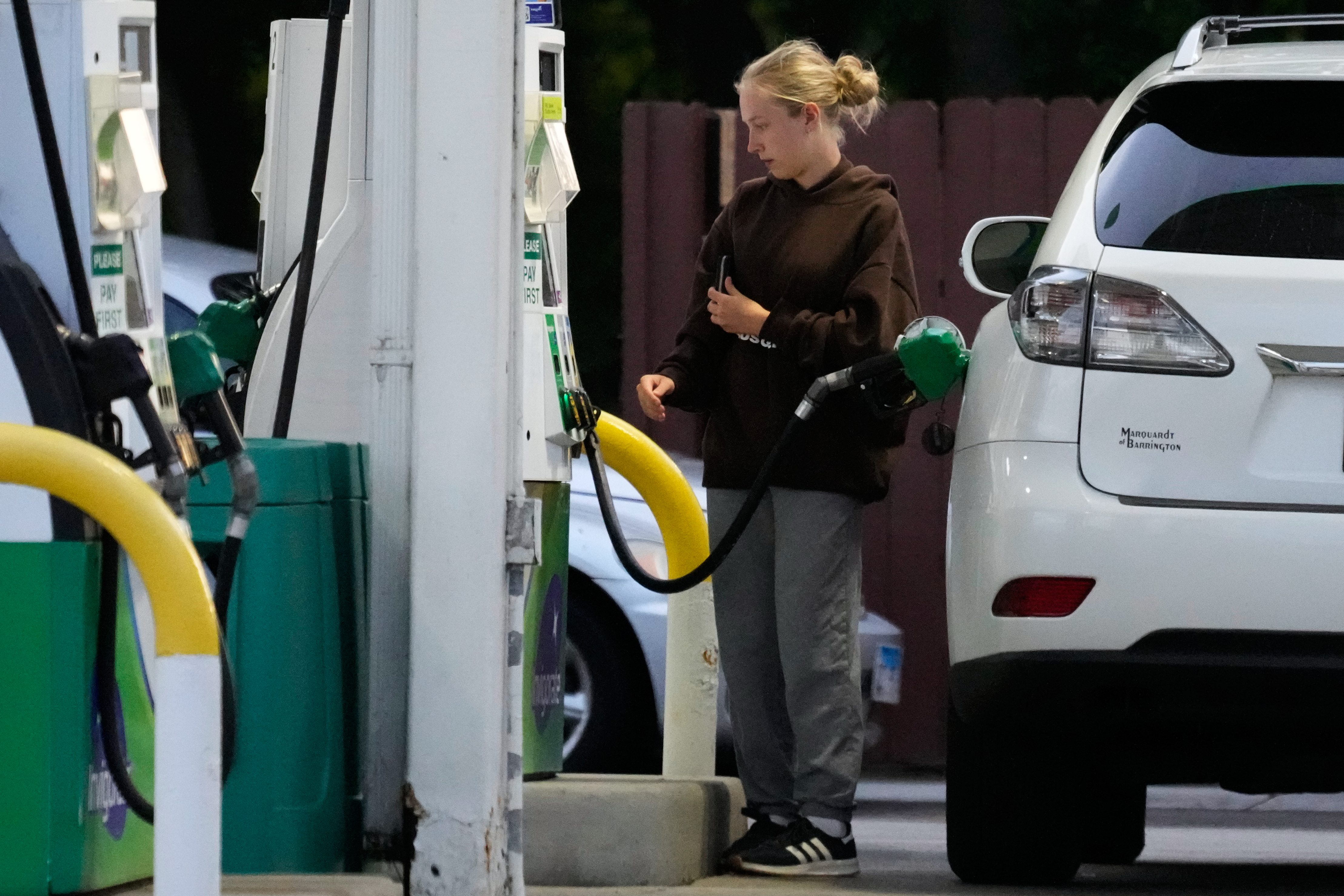 Woman refueling white vehicle at gas station with green and yellow fuel pump