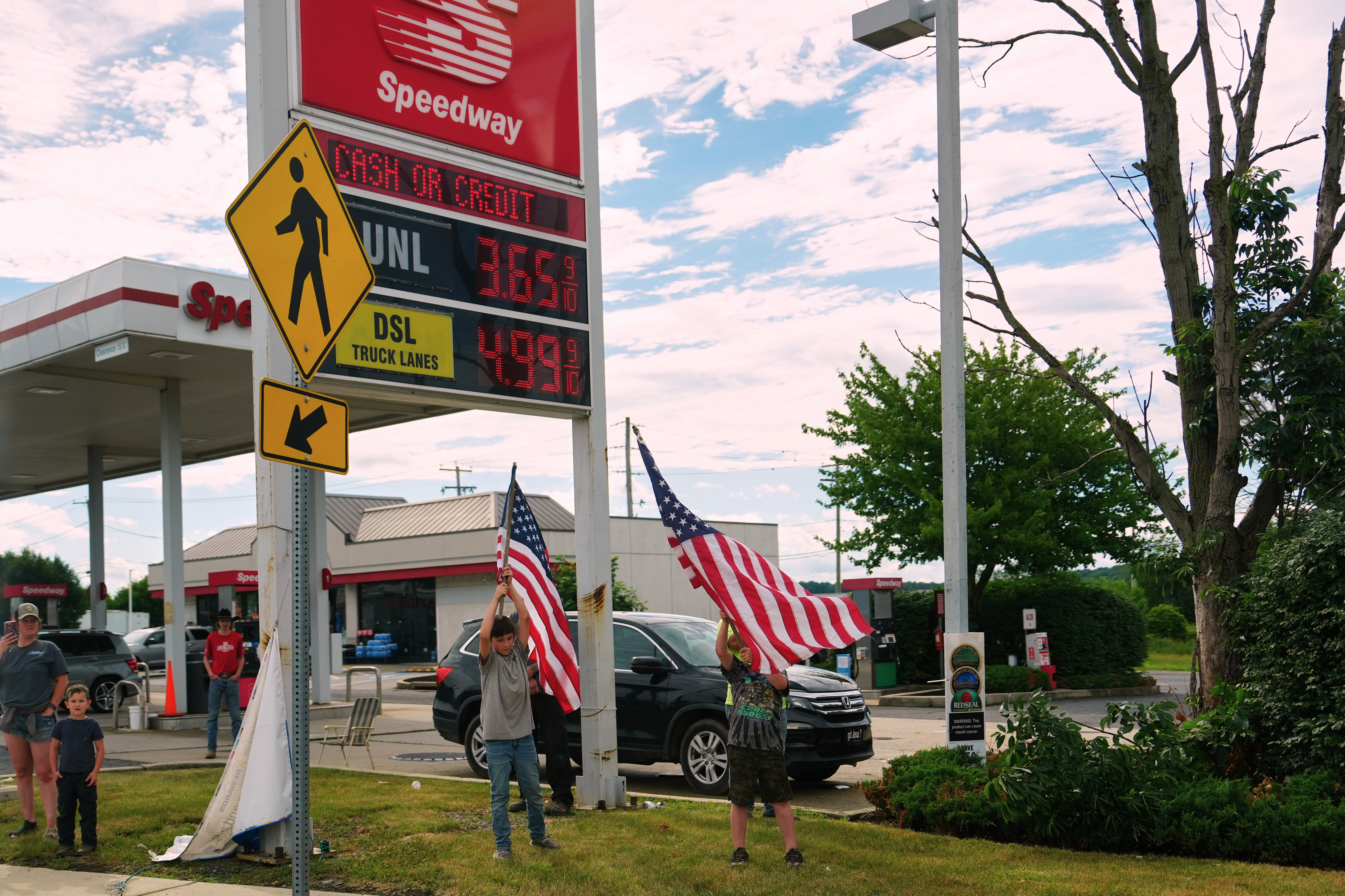 Speedway gas station with digital price display, American flags, and customers outside the storefront