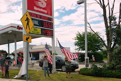 Speedway gas station with digital price display, American flags, and customers outside the storefront