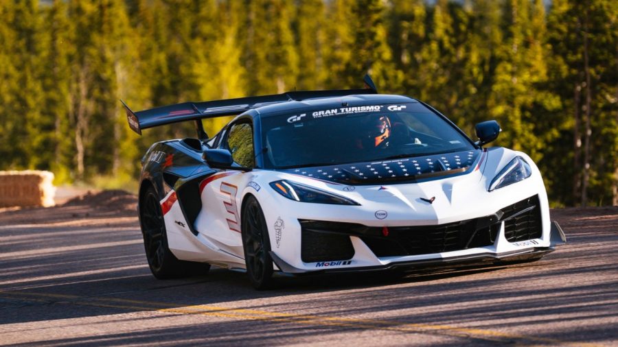 White and black Chevrolet Corvette C8 sports car with aerodynamic body kit parked on mountain road with forest backdrop