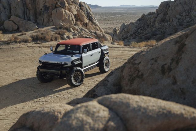 White and red GMC Hummer EV SUV parked in desert landscape surrounded by large boulders