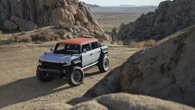 White and red GMC Hummer EV SUV parked in desert landscape surrounded by large boulders