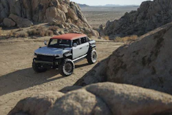 White and red GMC Hummer EV SUV parked in desert landscape surrounded by large boulders