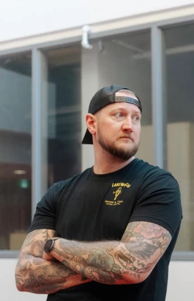 Man in black Lakers t-shirt with crossed arms standing in front of modern building
