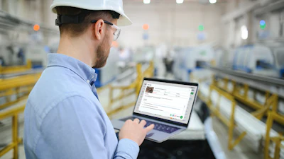 Industrial worker wearing hard hat and safety glasses using laptop in warehouse facility