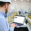 Industrial worker wearing hard hat and safety glasses using laptop in warehouse facility