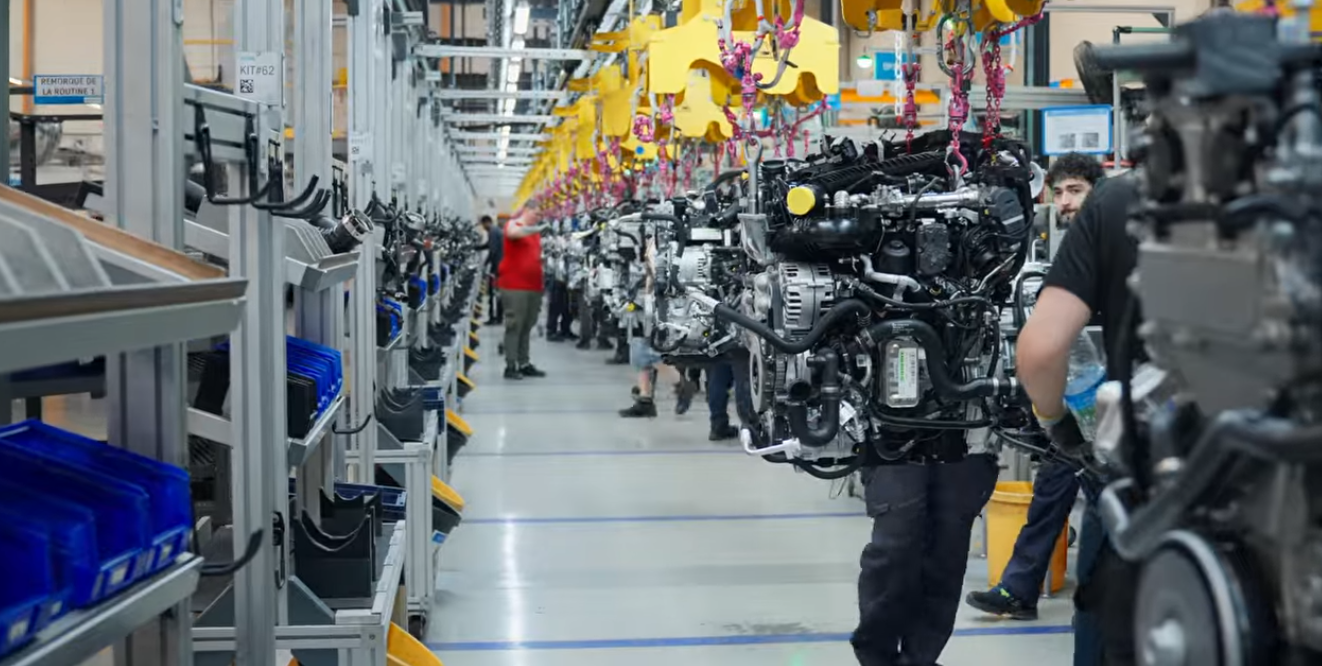 Automotive engine assembly line in manufacturing facility with workers and yellow safety equipment