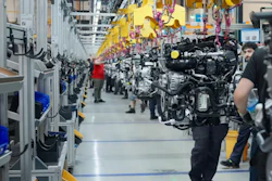 Automotive engine assembly line in manufacturing facility with workers and yellow safety equipment