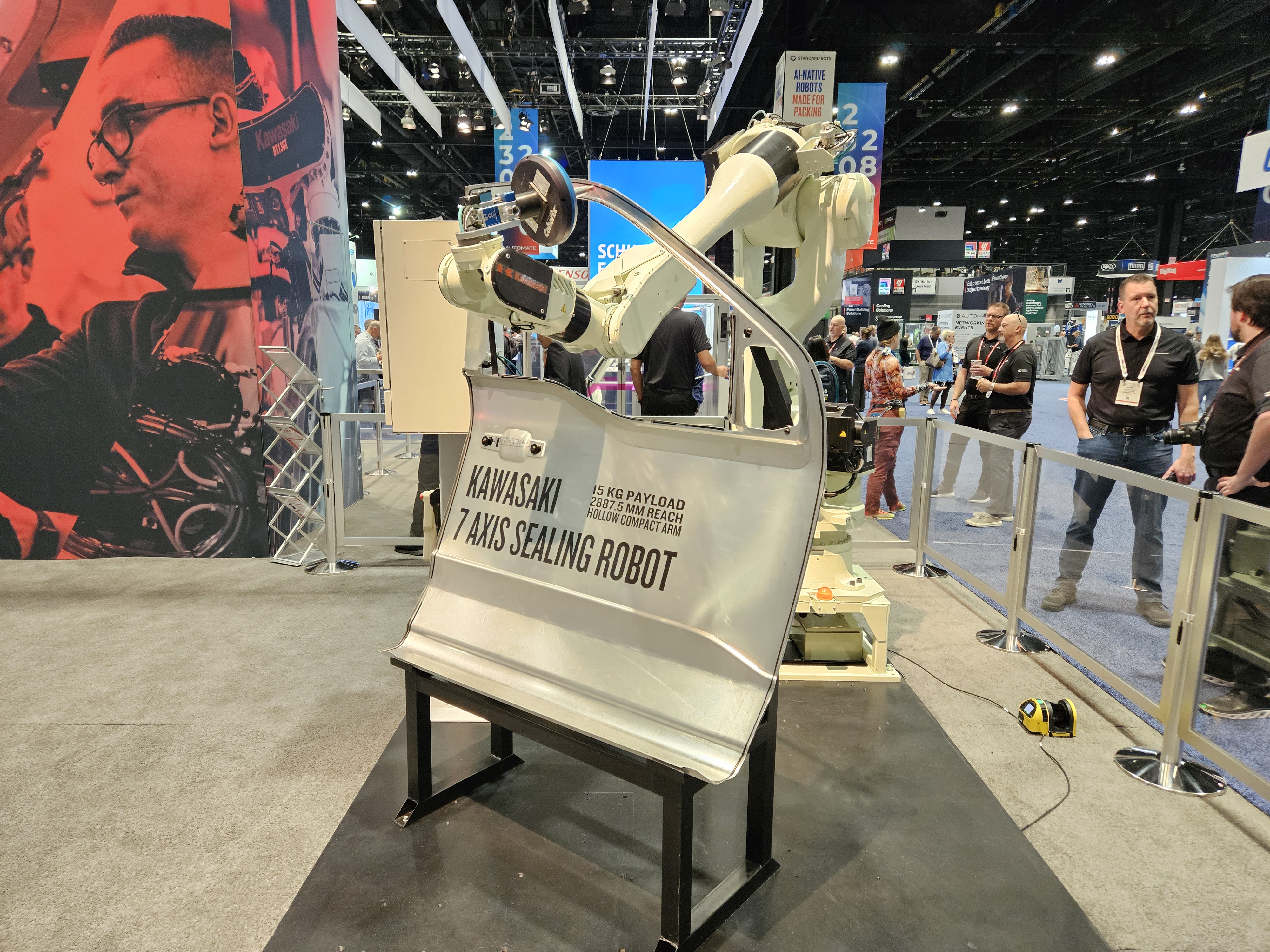Kawasaki Pano Sealing Robot on display at an industrial trade show with visitors in background