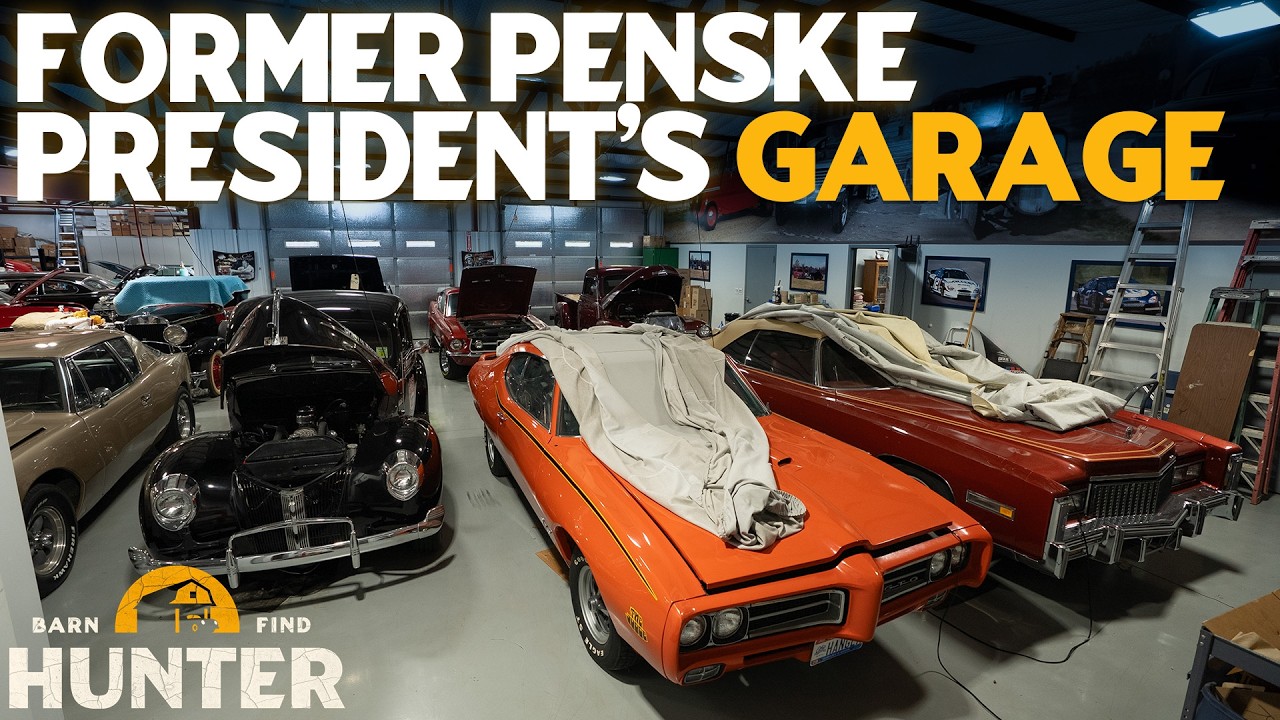 Classic and vintage cars displayed in a garage with white walls and fluorescent lighting, including an orange muscle car and maroon sedan.