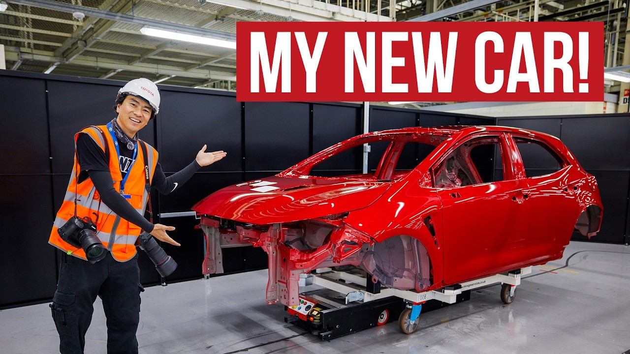 Factory worker in safety gear posing next to red car chassis in manufacturing facility