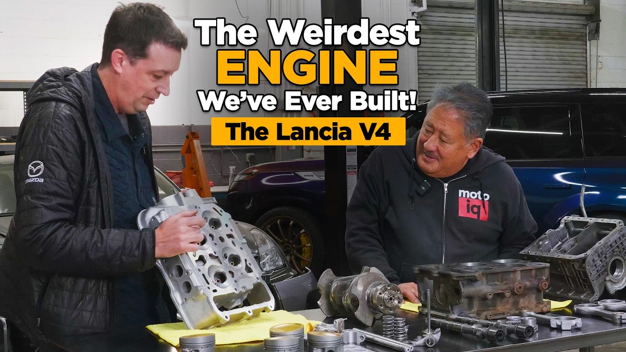 Two mechanics examine a Lancia V4 engine block in a workshop during an automotive documentary discussion.