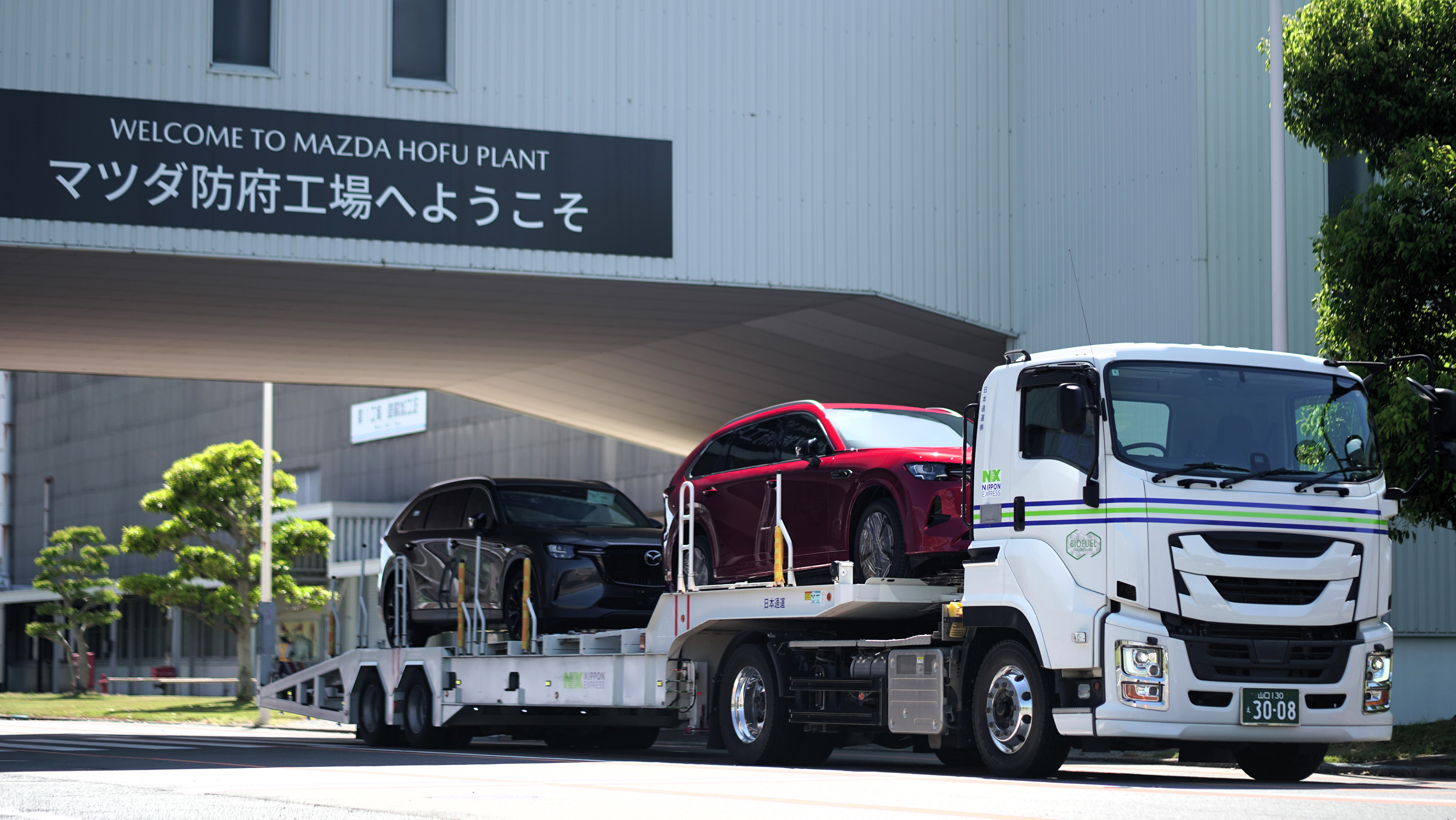 Mazda Hofu Plant entrance with white car carrier truck transporting red and black vehicles