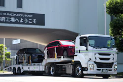Mazda Hofu Plant entrance with white car carrier truck transporting red and black vehicles