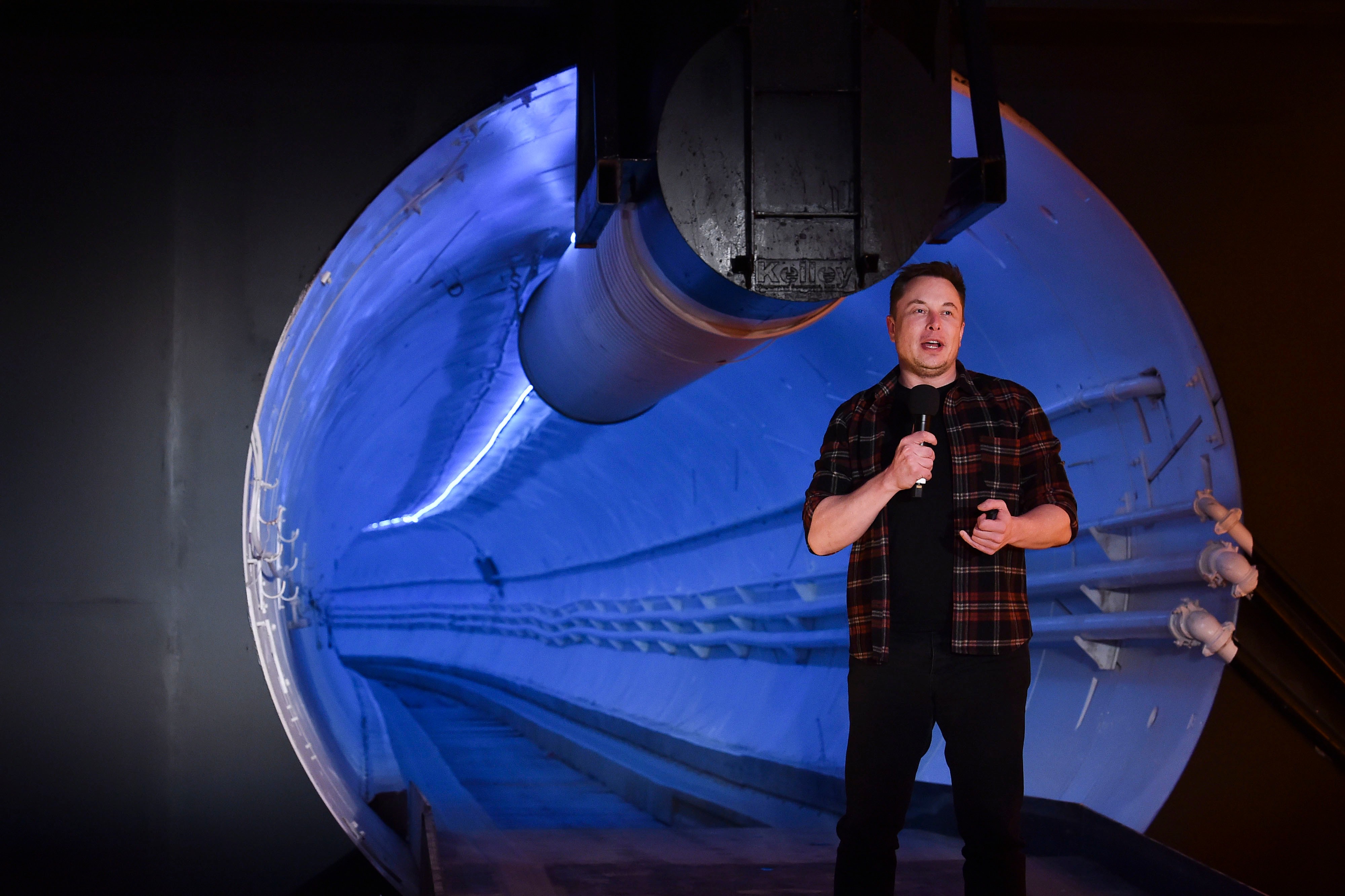 Man in plaid shirt presenting SpaceX Starship spacecraft model illuminated in blue light