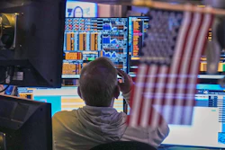 Trader monitoring financial markets on multiple data screens displaying stock charts and trading information