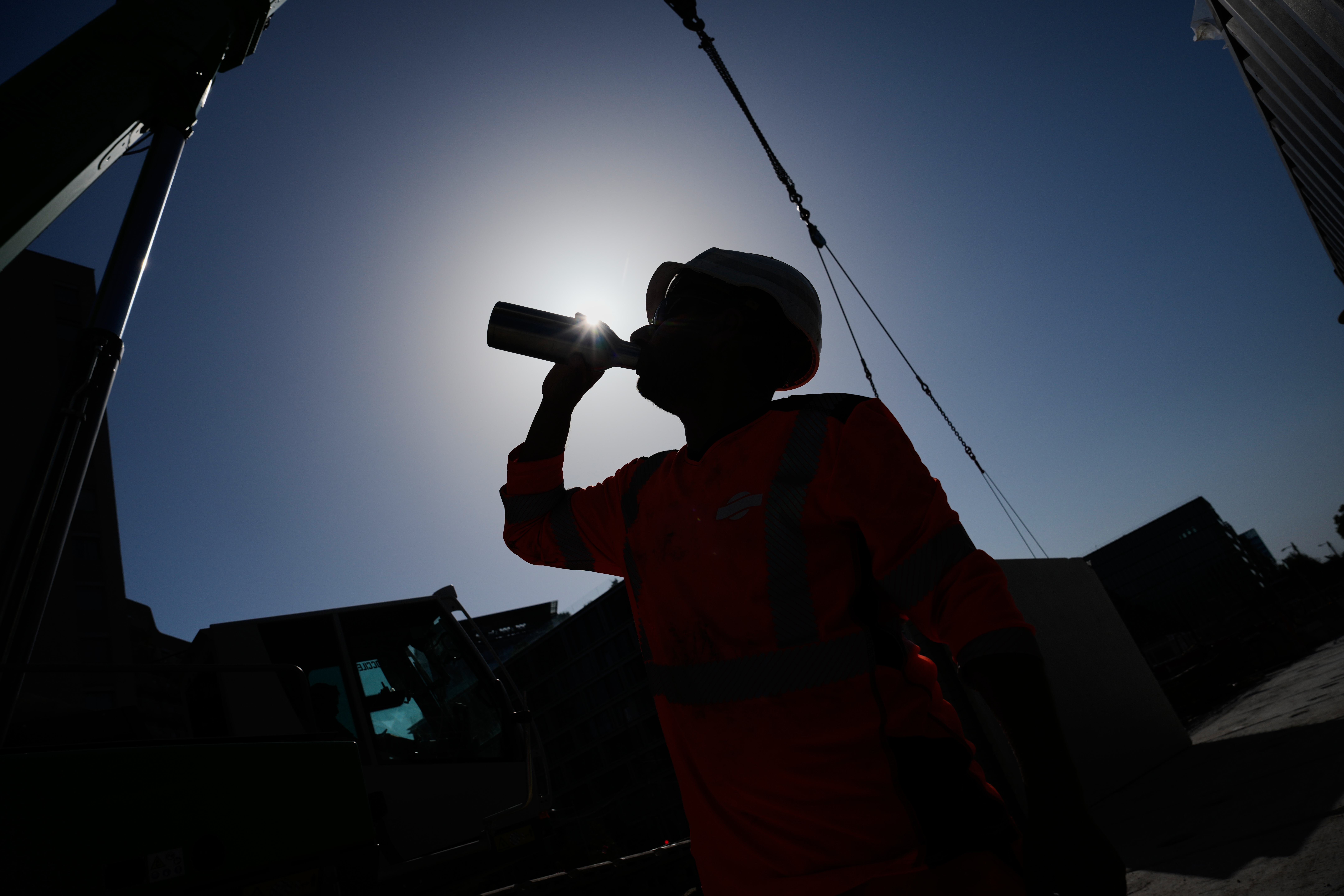 Silhouetted person drinking from a bottle against bright sky with buildings in background