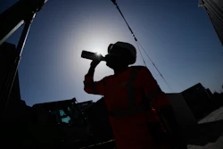 Silhouetted person drinking from a bottle against bright sky with buildings in background