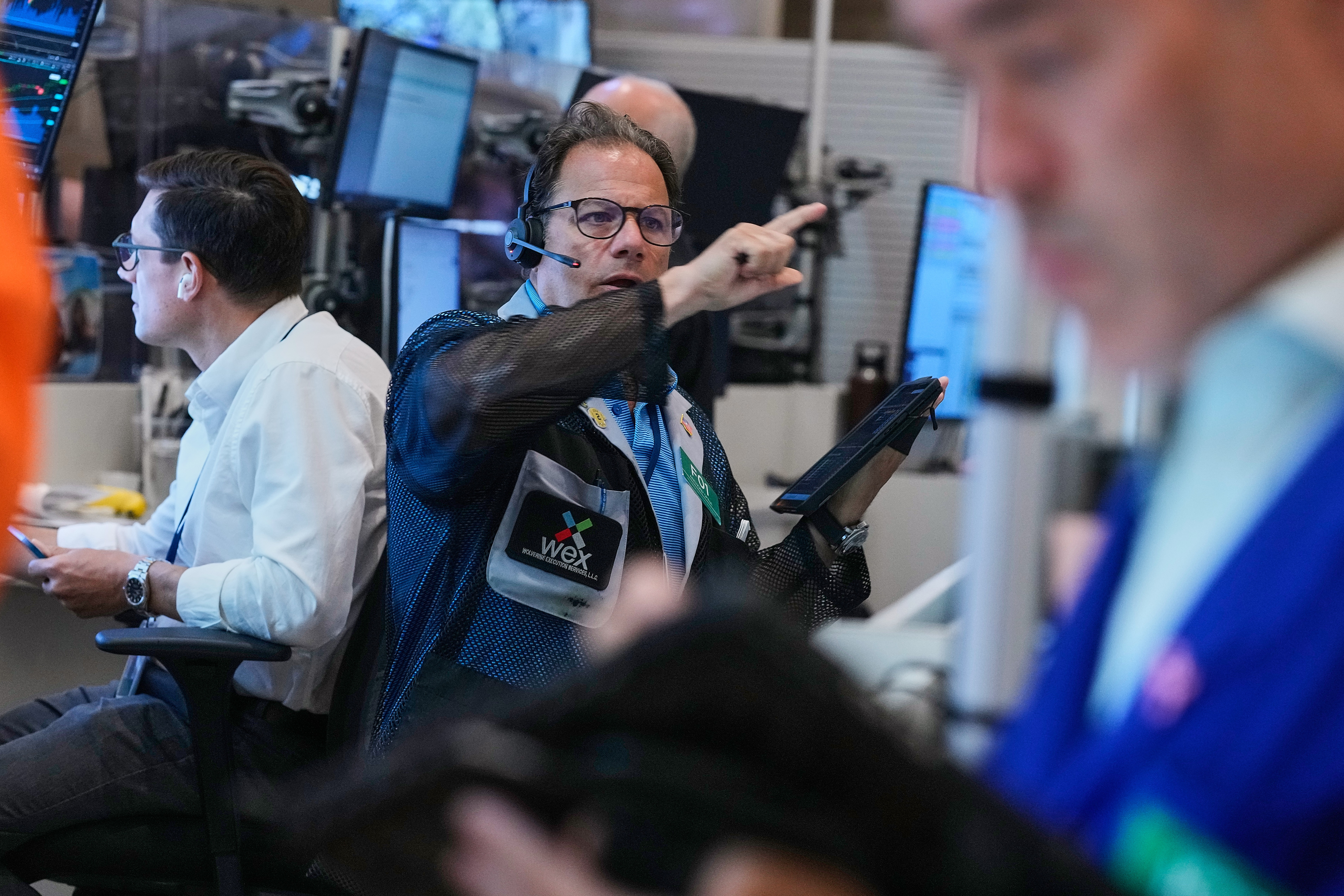 Trading floor professionals wearing headsets and credentials at computer workstations with multiple monitors