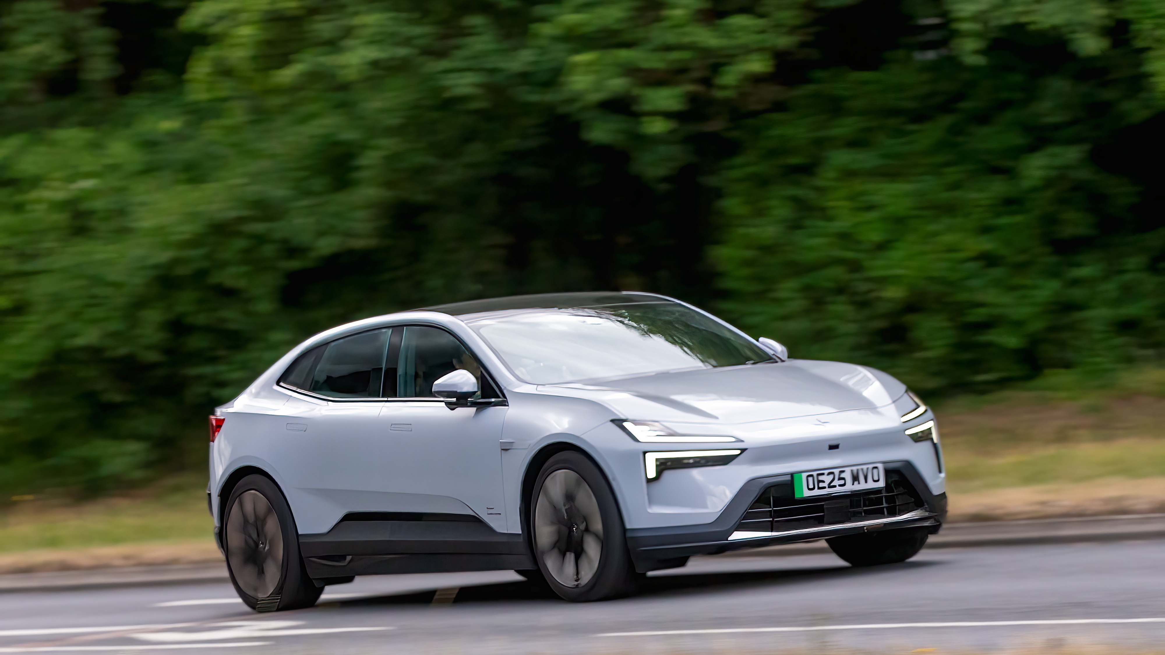 White Polestar electric SUV driving on a tree-lined road
