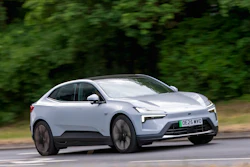 White Polestar electric SUV driving on a tree-lined road