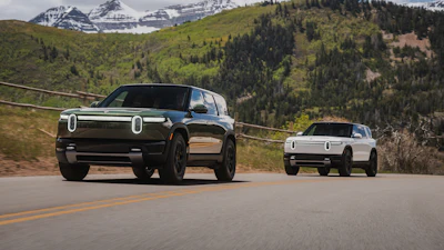 Two Rivian electric vehicles on a mountain road with snow-capped peaks and forested landscape in background