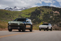 Two Rivian electric vehicles on a mountain road with snow-capped peaks and forested landscape in background