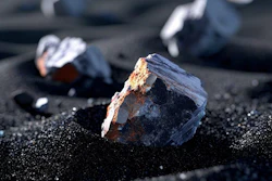 Dark mineral specimens with golden-brown crystals arranged on black sand with selective focus