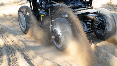 Vintage hot rod accelerating through sand with dramatic dust cloud billowing behind