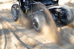 Vintage hot rod accelerating through sand with dramatic dust cloud billowing behind