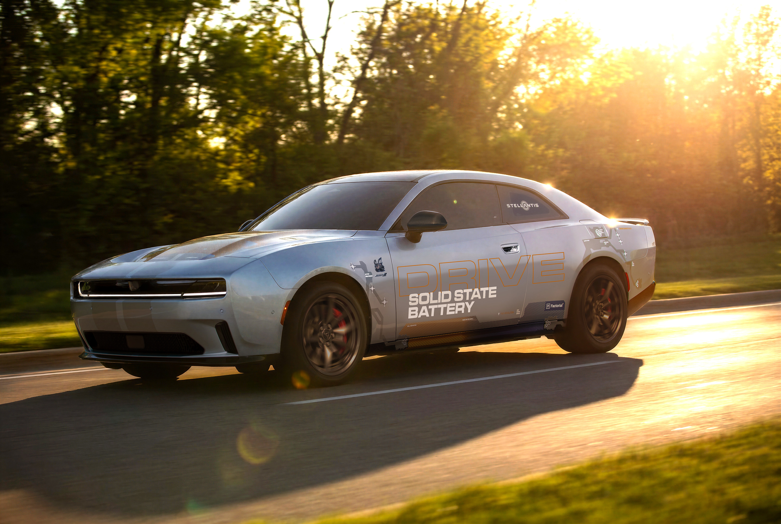 White Dodge Challenger muscle car with Solid State Battery branding driving on a tree-lined road at sunset