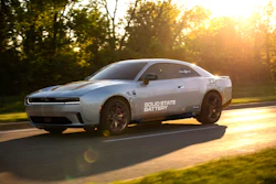 White Dodge Challenger muscle car with Solid State Battery branding driving on a tree-lined road at sunset