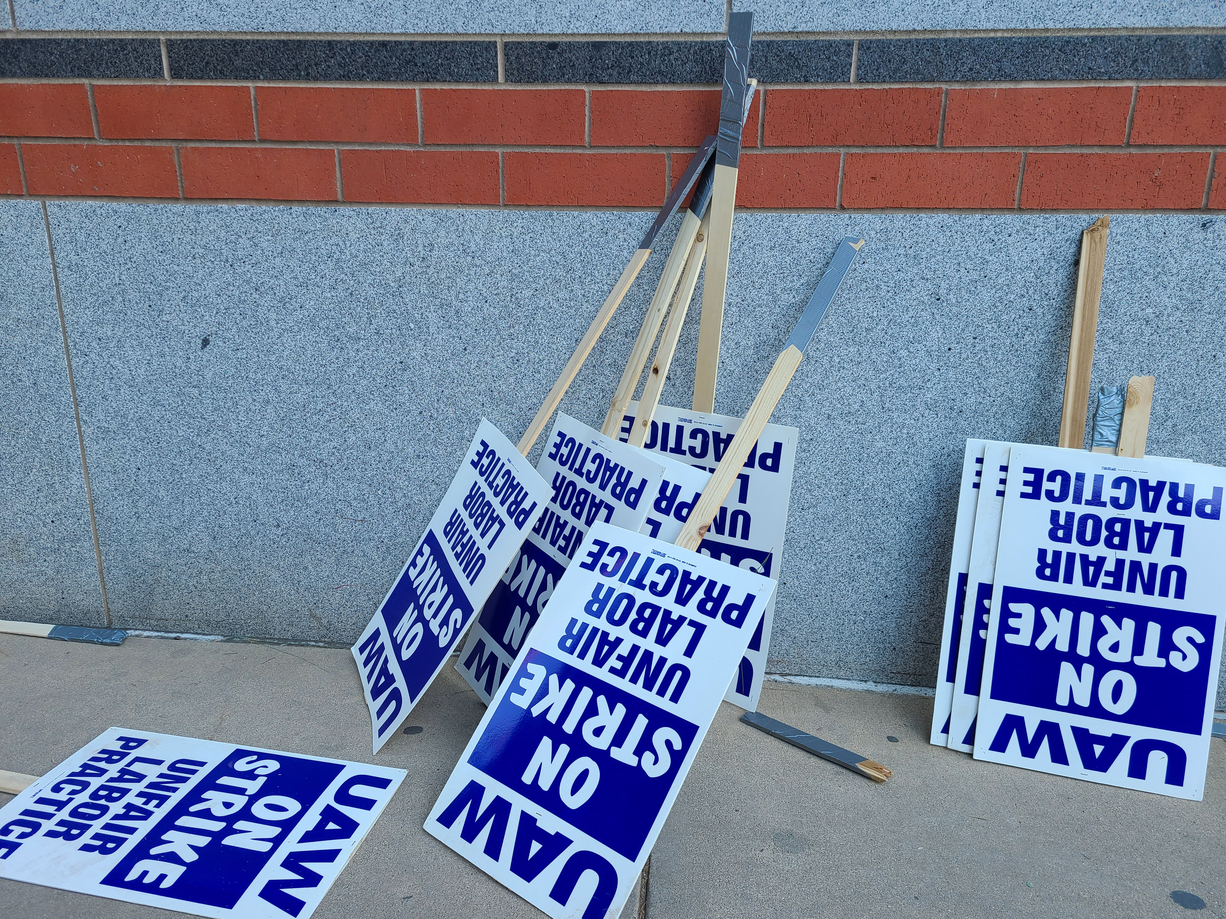 Blue and white protest signs reading 'NO STRIKE' leaning against brick wall with wooden handles