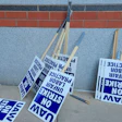 Blue and white protest signs reading 'NO STRIKE' leaning against brick wall with wooden handles