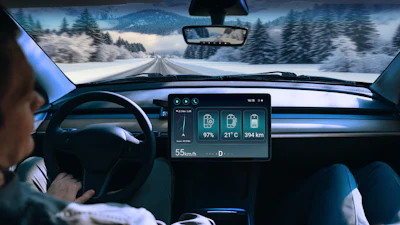 Driver's view of snowy mountain road with digital dashboard displaying speed, temperature, battery level, and distance traveled.
