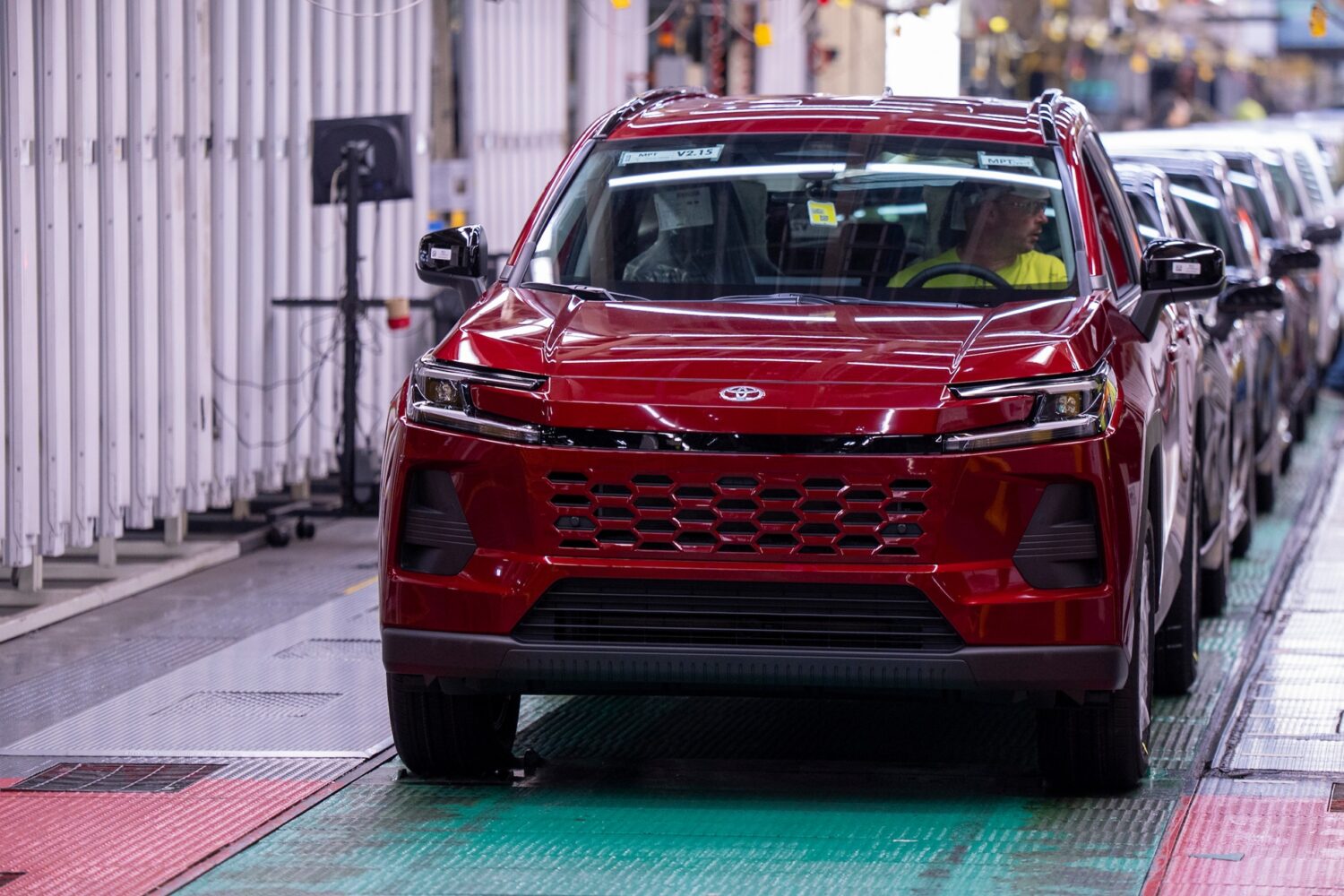 Red Toyota SUV on assembly line in manufacturing facility with quality control worker