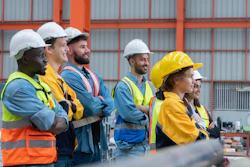 Construction team wearing safety gear standing together at industrial job site with metal building backdrop