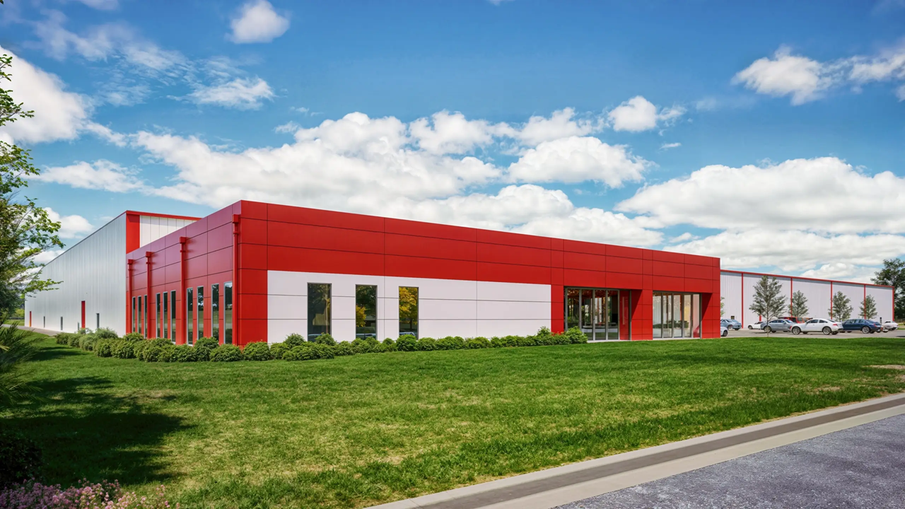 Modern red and white industrial building with large windows set on manicured green lawn under blue sky