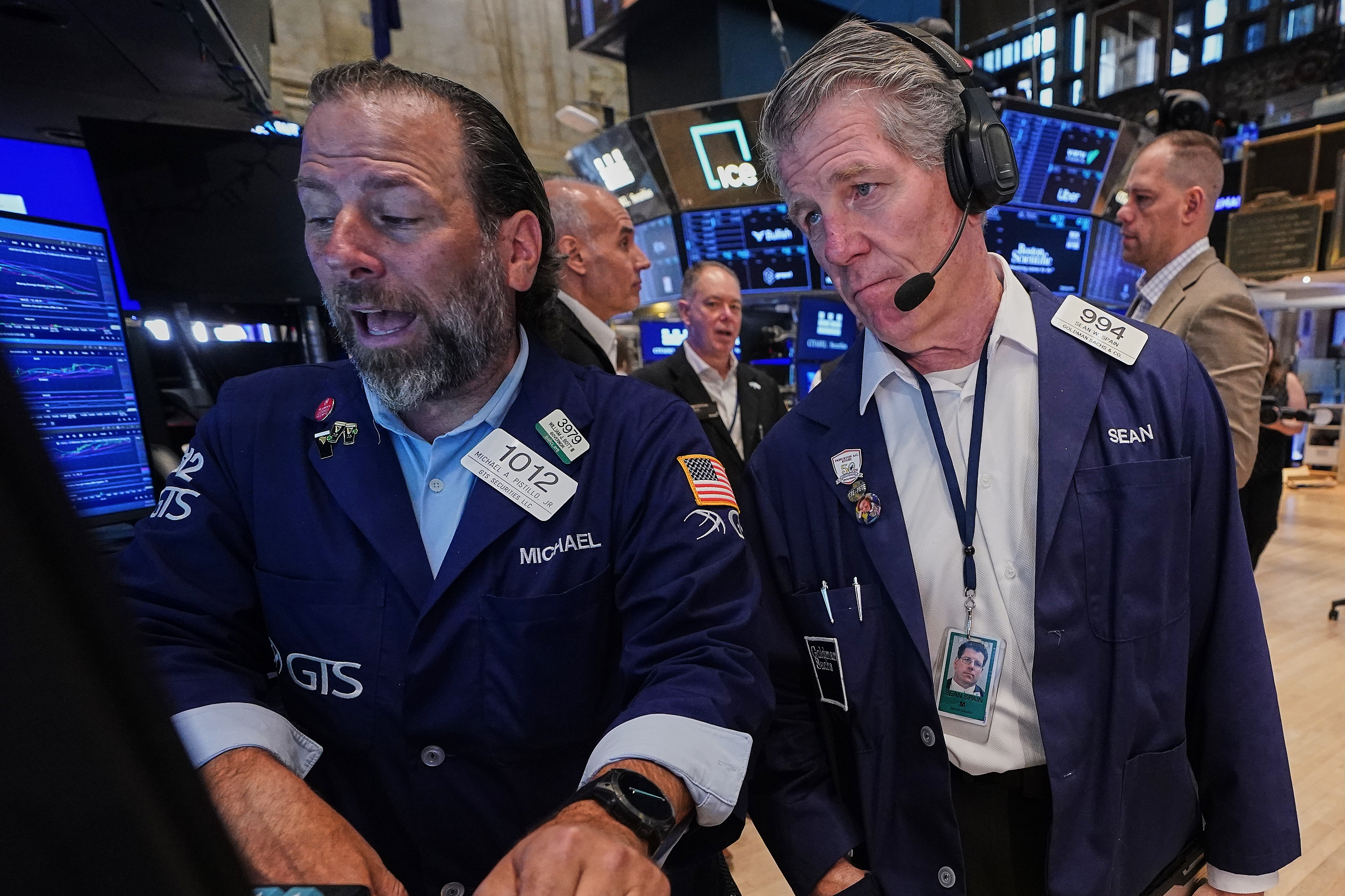 Stock exchange traders in navy blazers monitor market data on blue screens during trading session