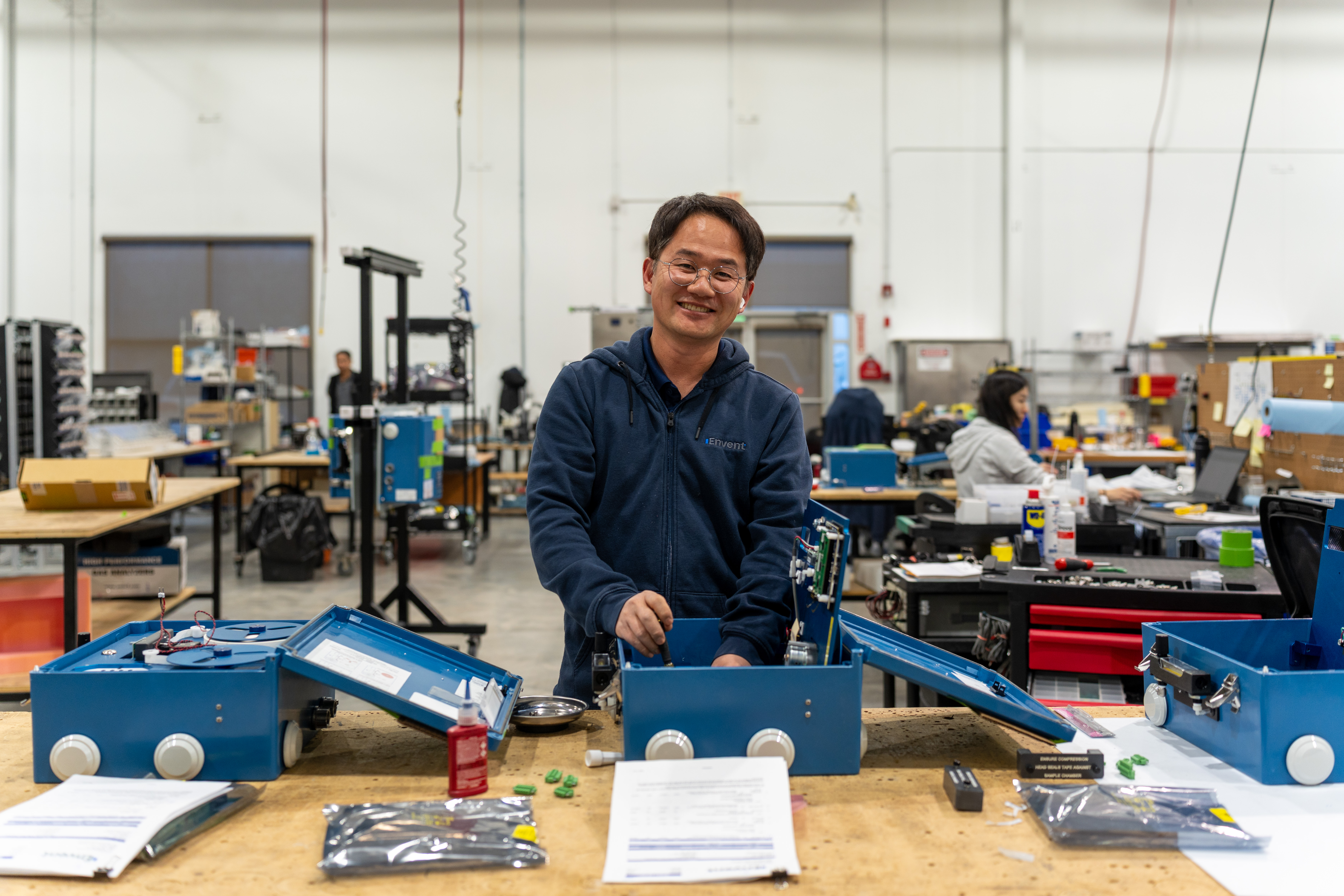 Man in navy jacket stands at workbench with blue toolboxes in a manufacturing workshop facility