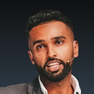 Professional headshot of a man with dark hair and beard wearing a light-colored shirt against a dark background