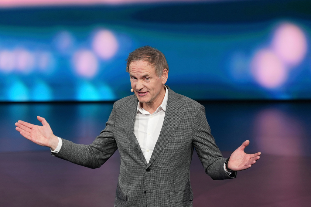 Professional man in gray blazer speaking at conference with animated hand gestures