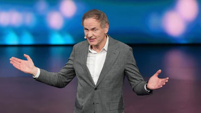Professional man in gray blazer speaking at conference with animated hand gestures