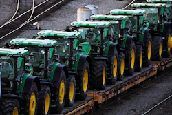 Row of green and yellow John Deere tractors loaded on a transport trailer
