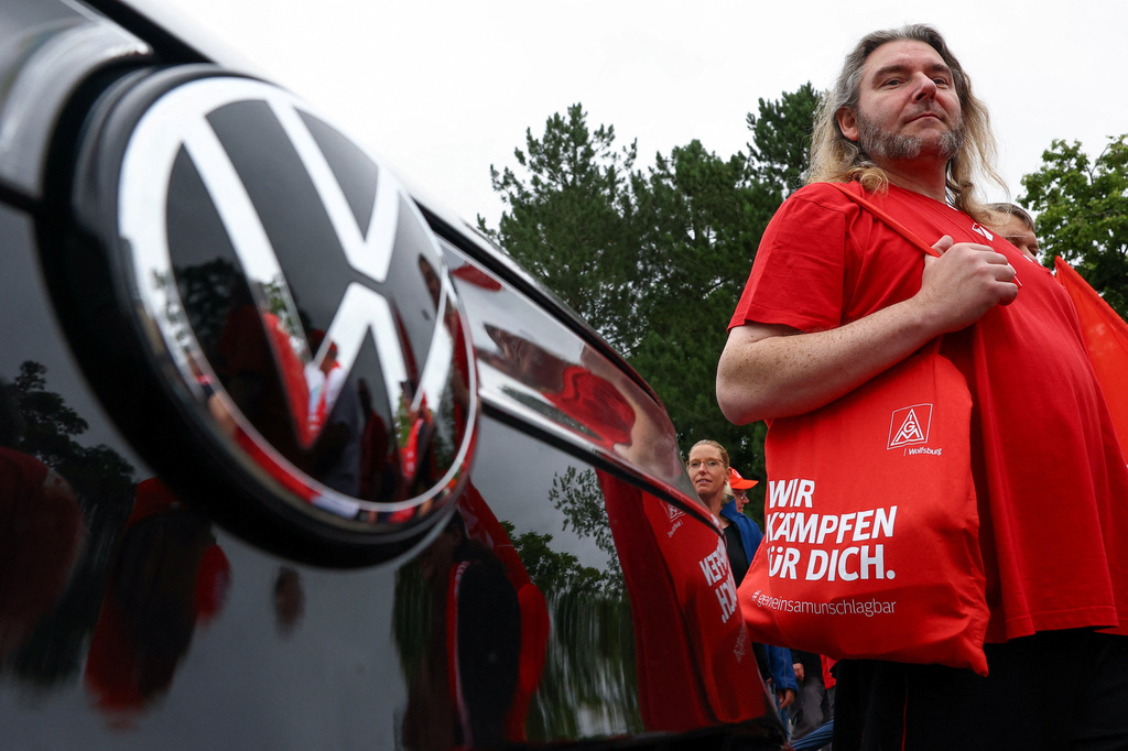 Man in red Volkswagen branded shirt standing beside vehicle with VW logo visible