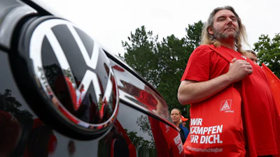 Man in red Volkswagen branded shirt standing beside vehicle with VW logo visible