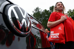 Man in red Volkswagen branded shirt standing beside vehicle with VW logo visible
