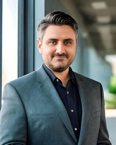 Professional headshot of a man in gray blazer and navy shirt smiling at camera