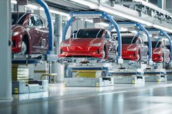 Red Tesla vehicles on automated assembly line with blue robotic arms in modern manufacturing facility